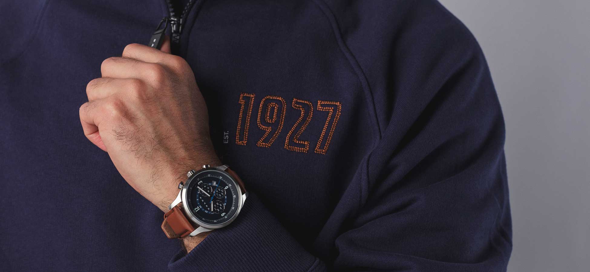 Person wearing blue 1927 half zip sweater and brown leather watch from Volvo merchandise