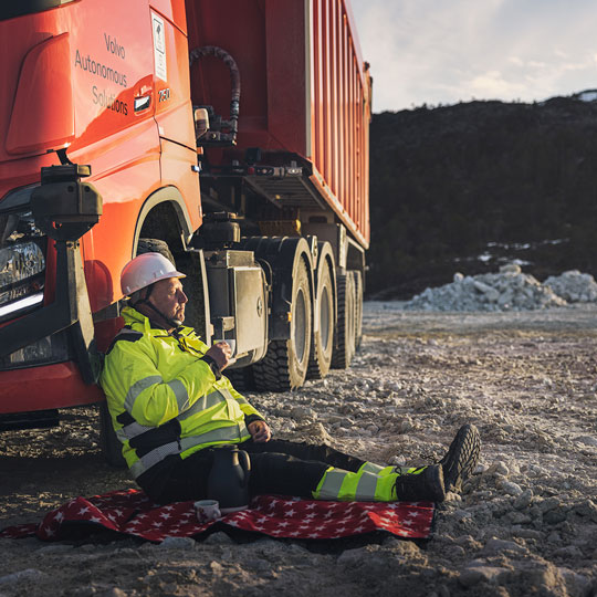 Man in high vis workwear leaning against a red Volvo vehicle.